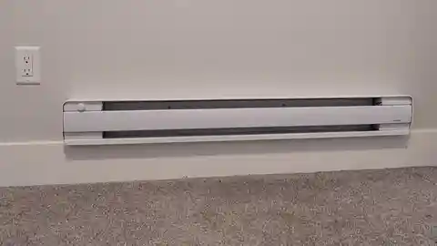 White electric baseboard heater with built-in thermostat next to outlet