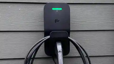 Black wall-mounted EV charger with green status light on gray siding