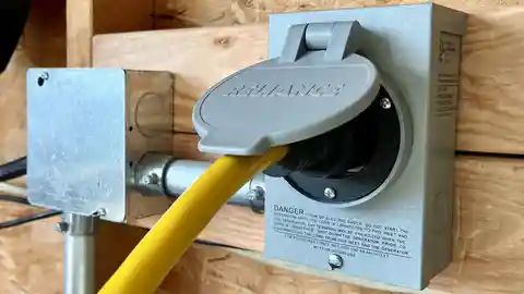 Yellow power cord plugged into generator inlet box on OSB plywood wall