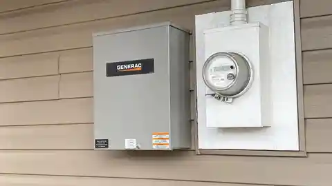 Gray Generac transfer switch mounted next to electrical meter on siding