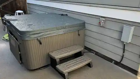 Beachcomber hot tub on patio with dedicated electrical panel on house siding