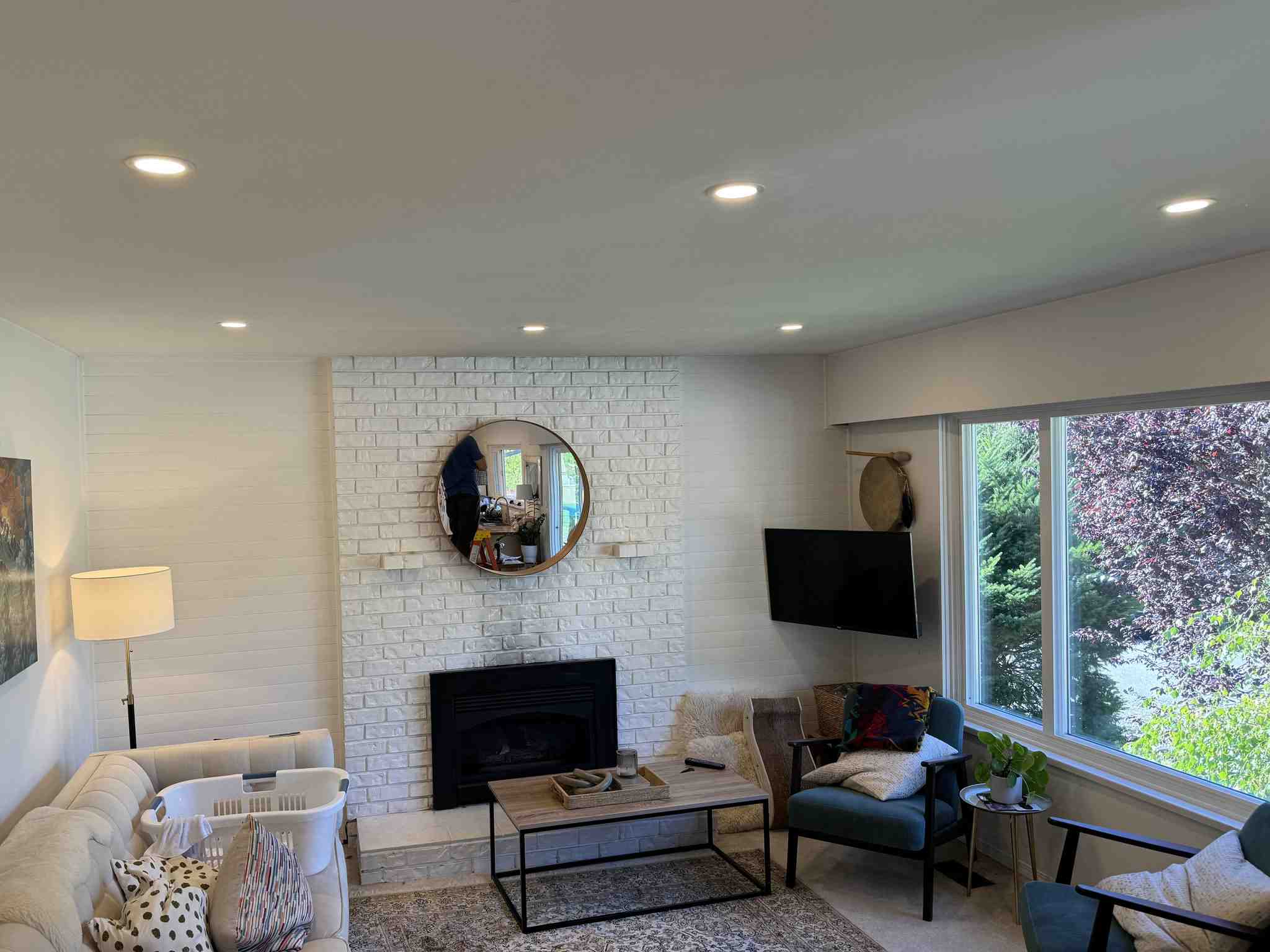 Modern living room with recessed LED pot lights, white brick fireplace, and large windows