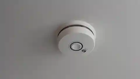 White smoke detector mounted on ceiling in hallway